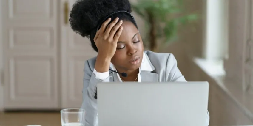 Fatigued businesswoman wearing a headset resting her head on her hand with eyes closed at her laptop
