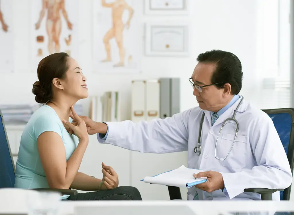 Doctor palpating the front of a woman's neck to examine her thyroid gland during a Hashimoto's disease evaluation