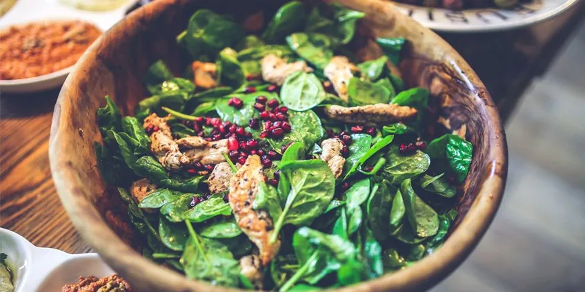 Fresh spinach salad with grilled chicken and pomegranate seeds in a wooden bowl