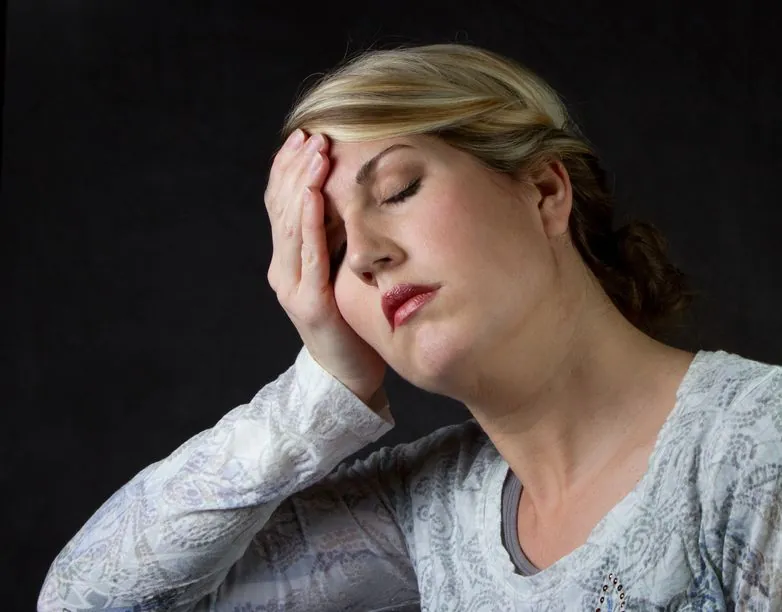 Woman pressing her fingers to her temples with a headache — one of the overlapping symptoms women often dismiss during perimenopause