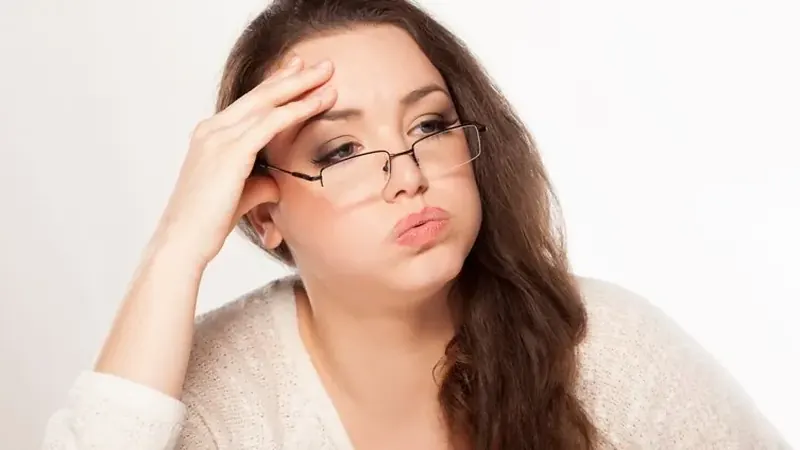 Tired woman wearing glasses exhales with her hand pressed to her forehead — fatigue is a common symptom of thyroid imbalance