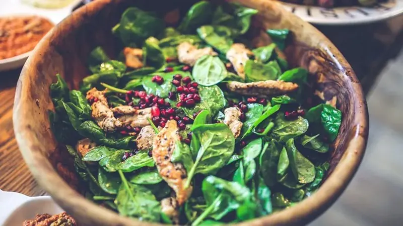 Fresh spinach salad with grilled chicken and pomegranate seeds in a wooden bowl