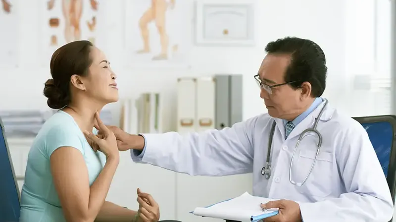 Doctor palpating the front of a woman's neck to examine her thyroid gland during a Hashimoto's disease evaluation
