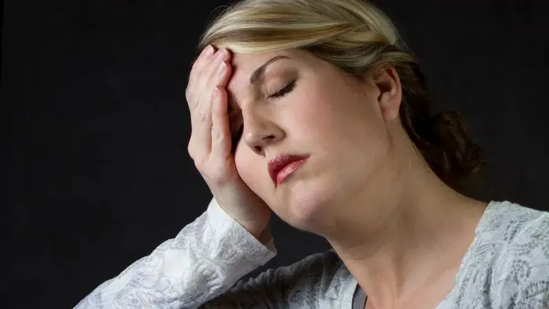 Woman pressing her fingers to her temples with a headache — one of the overlapping symptoms women often dismiss during perimenopause