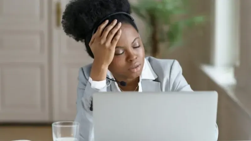 Fatigued businesswoman wearing a headset resting her head on her hand with eyes closed at her laptop